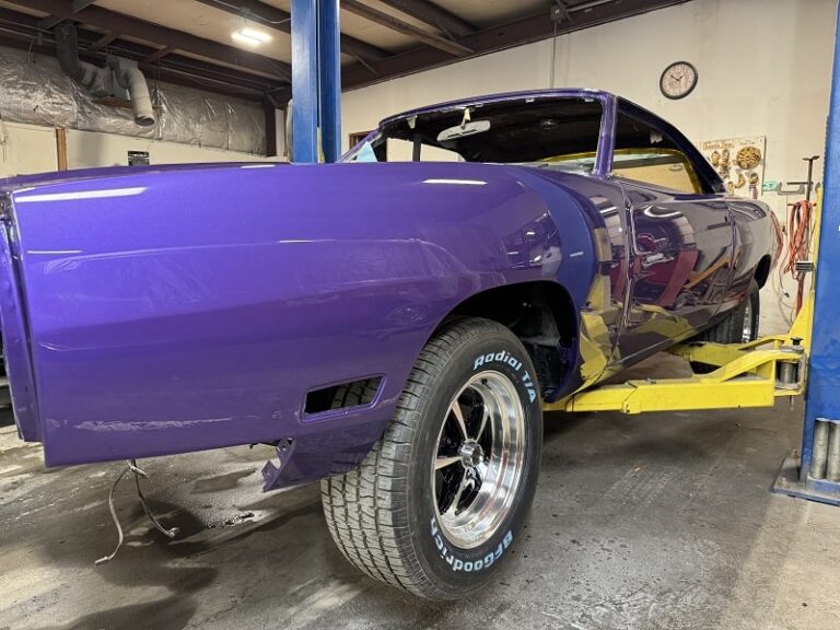Vintage purple muscle car undergoing restoration process in workshop.