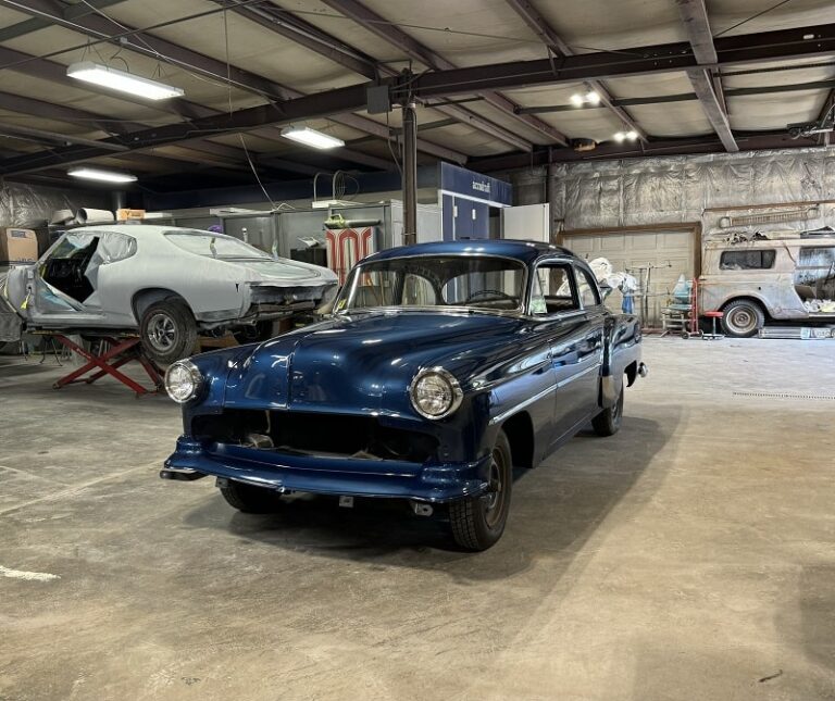 Vintage blue classic car undergoing restoration in a workshop.