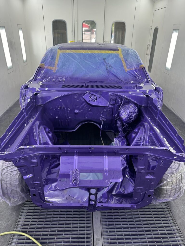 Car body painted purple, inside a professional spray booth, ready for assembly.