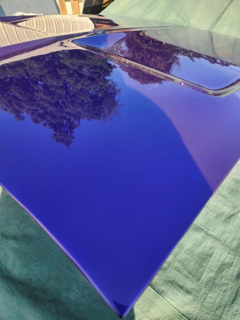 Blue car hood with reflective surface showing tree reflection.