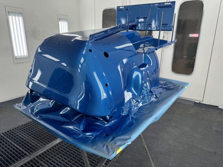 Restored blue car body shell in a professional paint booth at John's Automotive.