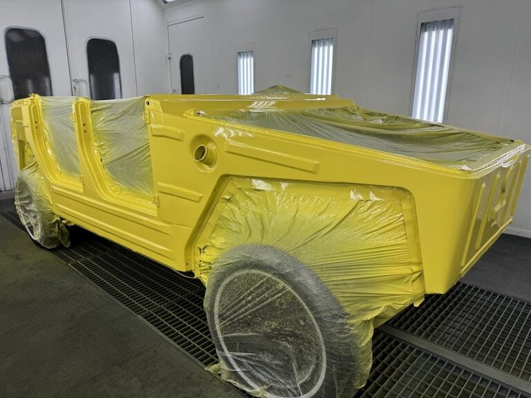 Restoring a classic car body with yellow primer in a professional auto body shop.