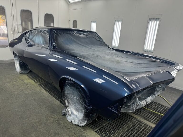 Restoring a vintage muscle car with a fresh coat of dark blue paint in a professional auto body shop.