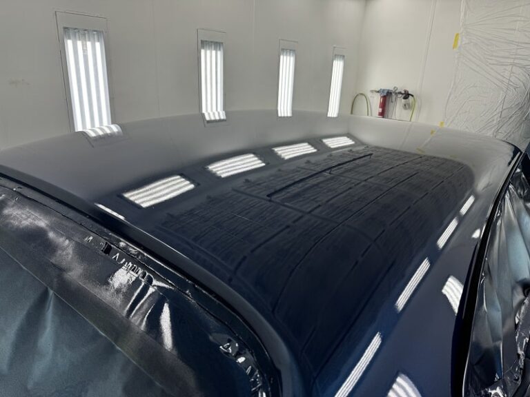 Close-up of a black car's roof in a professional auto body shop.