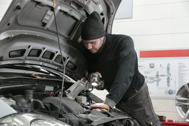 Technician inspecting car engine during fuel system check at John's Auto Restoration.