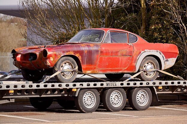 Old rusty car on flatbed trailer for transport.