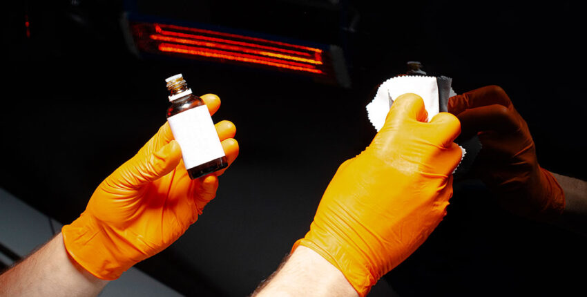 Hands applying pinstriping to a car with orange gloves for vehicle enhancement.