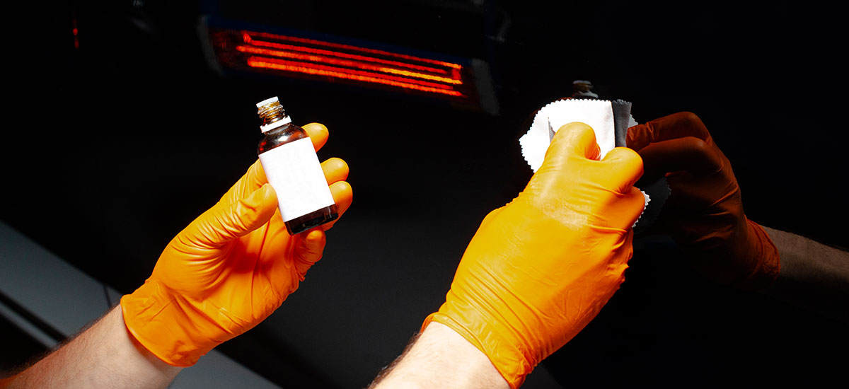 Hands applying pinstriping to a car with orange gloves for vehicle enhancement.
