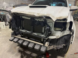 Front view of a damaged white pickup truck with missing grille and bumper.