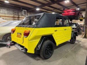 Restored yellow off-road vehicle in auto shop with other cars and equipment.