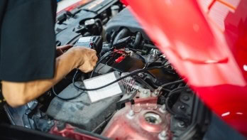 Technician performing vehicle diagnostics in a car engine bay.
