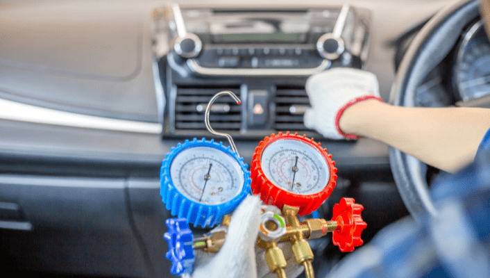 Technician performing air conditioning recharge with gauges inside a vehicle.