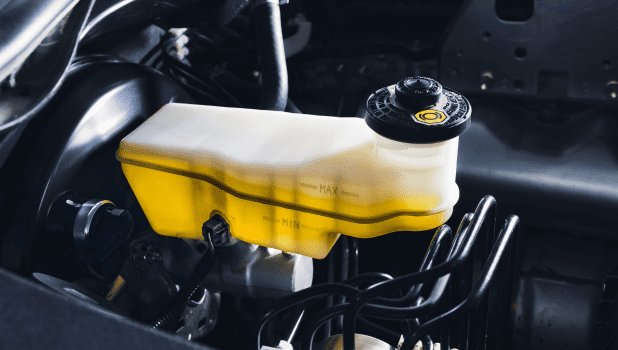 Close-up of a yellow brake fluid reservoir in a vehicle engine bay.