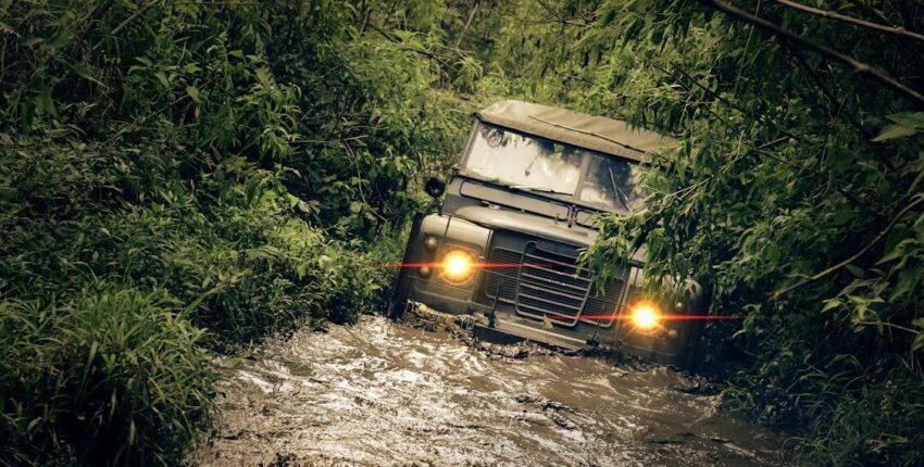 Off-road 4x4 vehicle navigating through muddy trail surrounded by dense greenery.