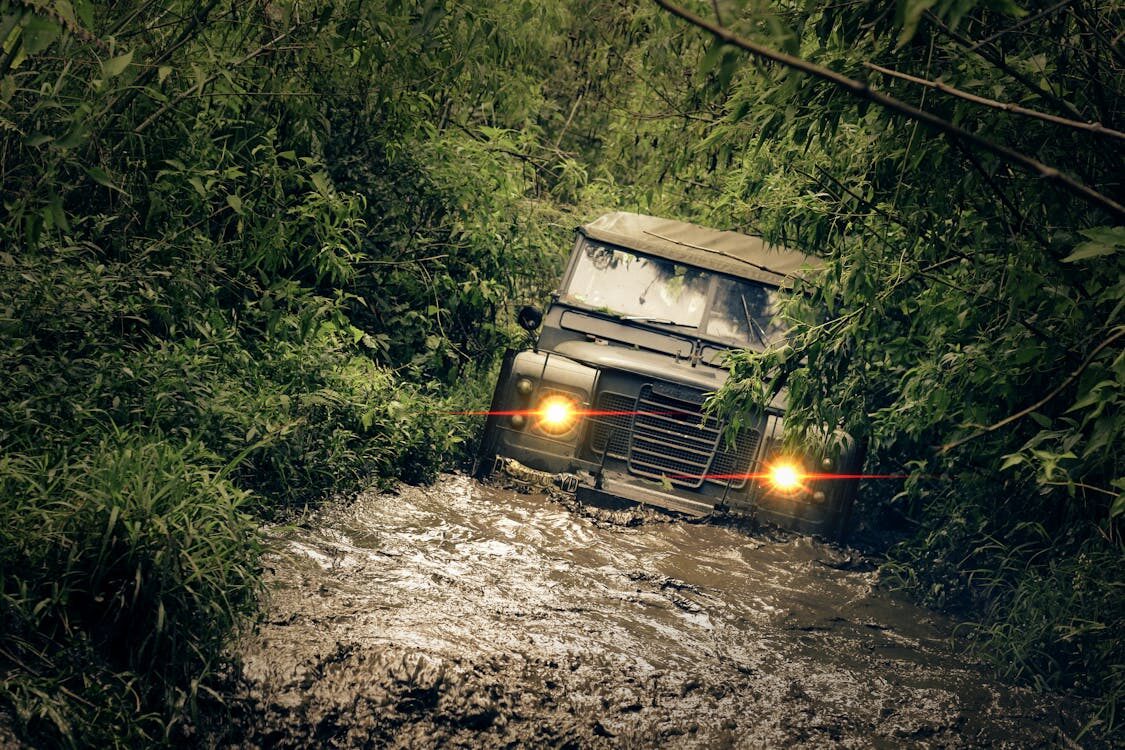 Off-road 4x4 vehicle navigating through muddy trail surrounded by dense greenery.
