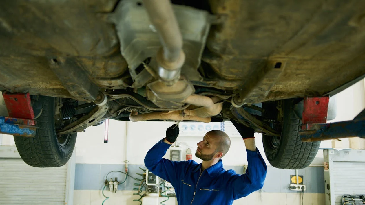 Automotive mechanic inspecting the underside of a vehicle in a repair shop.