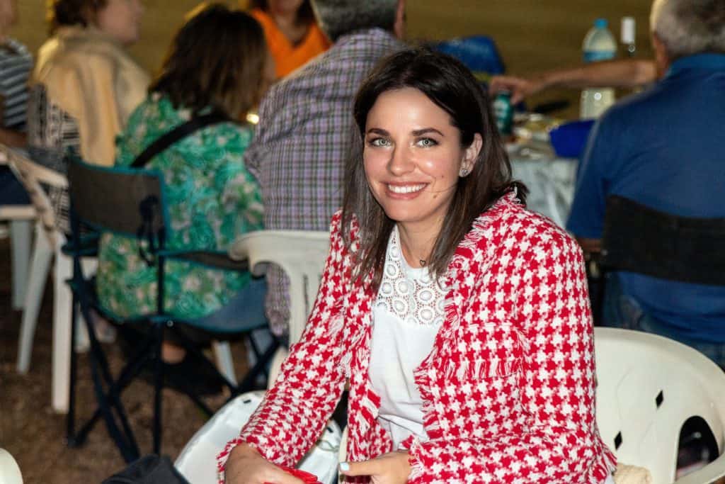 Encuentro social en interior con mujer sonriendo, rodeada de personas en mesa, en evento informal, en ambiente cálido y amigable, fotografía de alta calidad para promociones y artículos de blog.