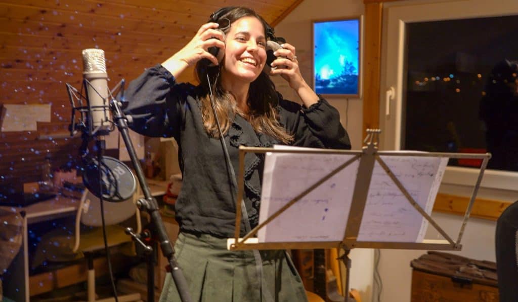 Disfrutando en un estudio de grabación, una mujer joven canta y graba música en un entorno acogedor con madera en las paredes y equipamiento profesional.