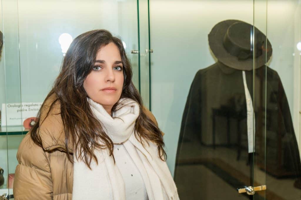 Mujer visitando museo en Lucca, Italia, con exhibición de sombrero antiguo en vitrina.