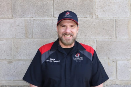 Friendly auto service technician at Legacy Tire & Auto Repair smiling outdoors.