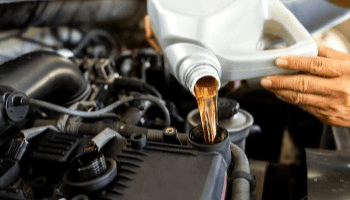 Technician pouring engine oil into a car engine during maintenance.