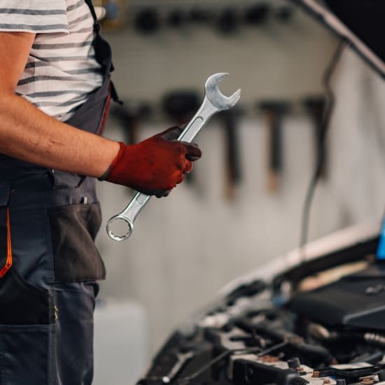 Auto mechanic holding a wrench near a car engine for repair or maintenance.