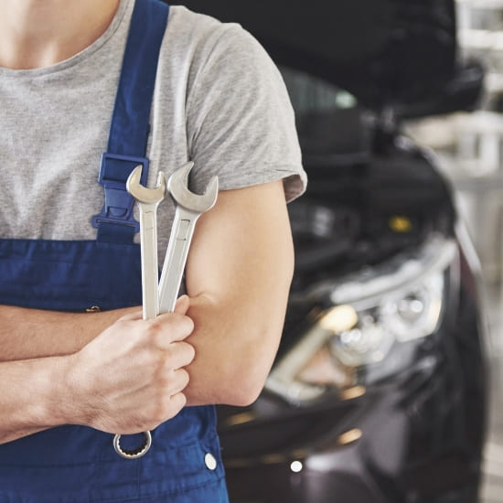 Auto repair technician holding wrenches in front of a car at service center.