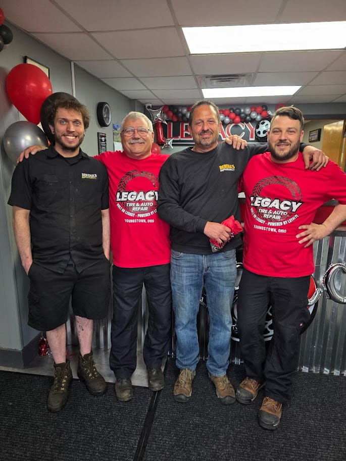Team of mechanics and staff at Legacy Tire & Auto Repair in front of service area.