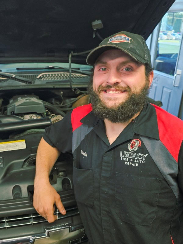 Happy mechanic at Legacy Tire & Auto Repair with open car hood.
