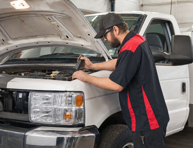 Technician inspecting engine of a white pickup truck at Legacy Tire.