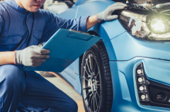 Skilled technician inspecting a blue car's headlight during engine repair.