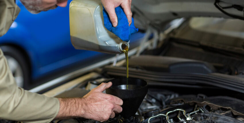 Auto mechanic pouring oil into car engine during maintenance.