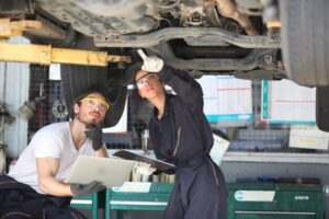 Vehicle maintenance technicians inspecting car undercarriage for issues.