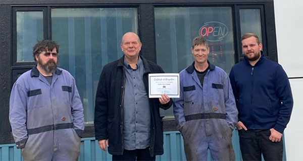 L Stop Auto team with certificate outside the shop.