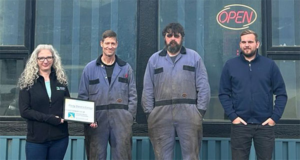 L Stop Auto team standing outside the shop with an "Open" sign.