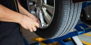 Technician repairing car tire on lift at auto shop.
