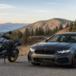 Car and motorcycle parked on mountain road with scenic landscape.