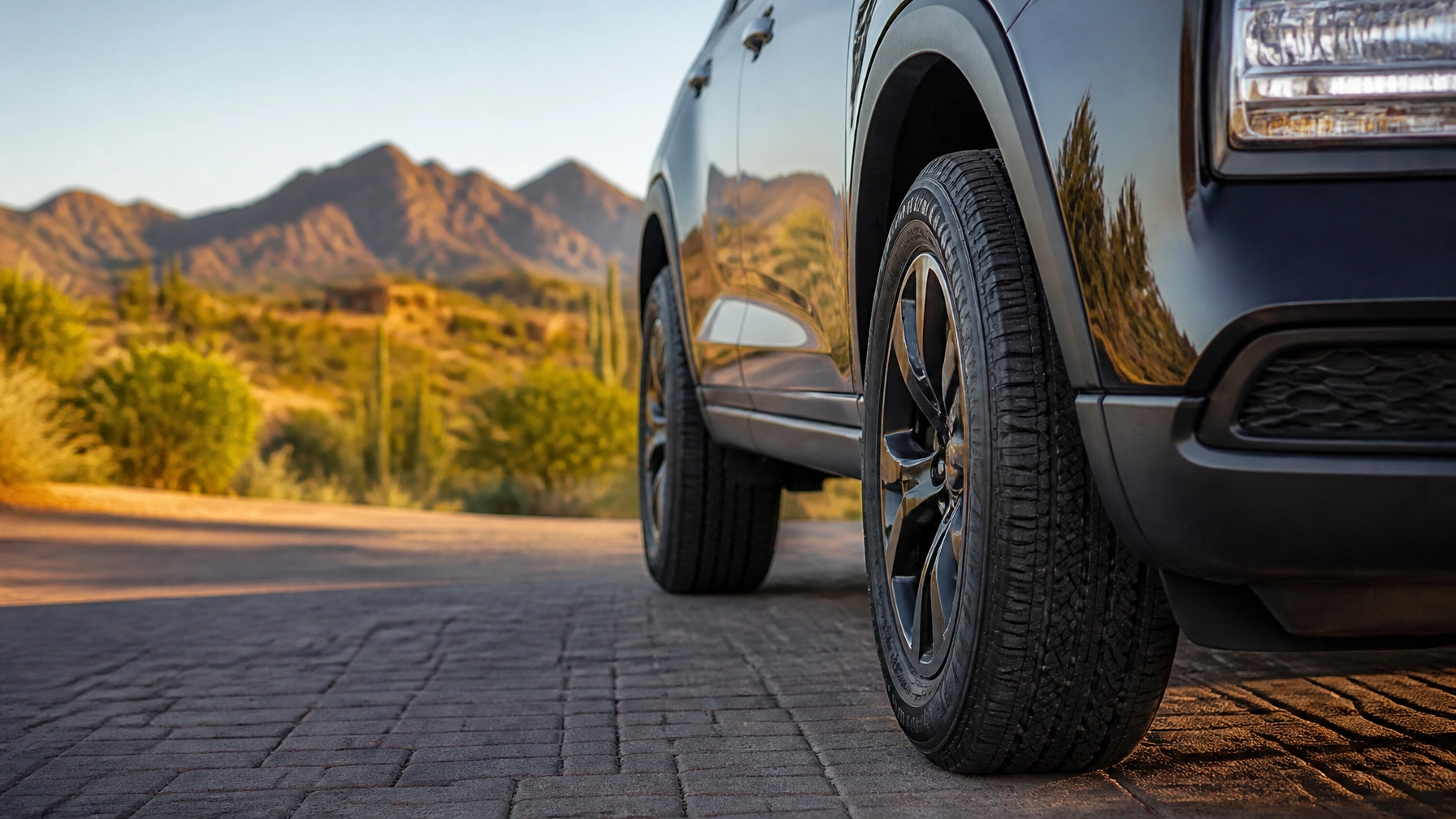 Close-up of a black SUV tire at Macy's Tire & Lube with mountain landscape background.