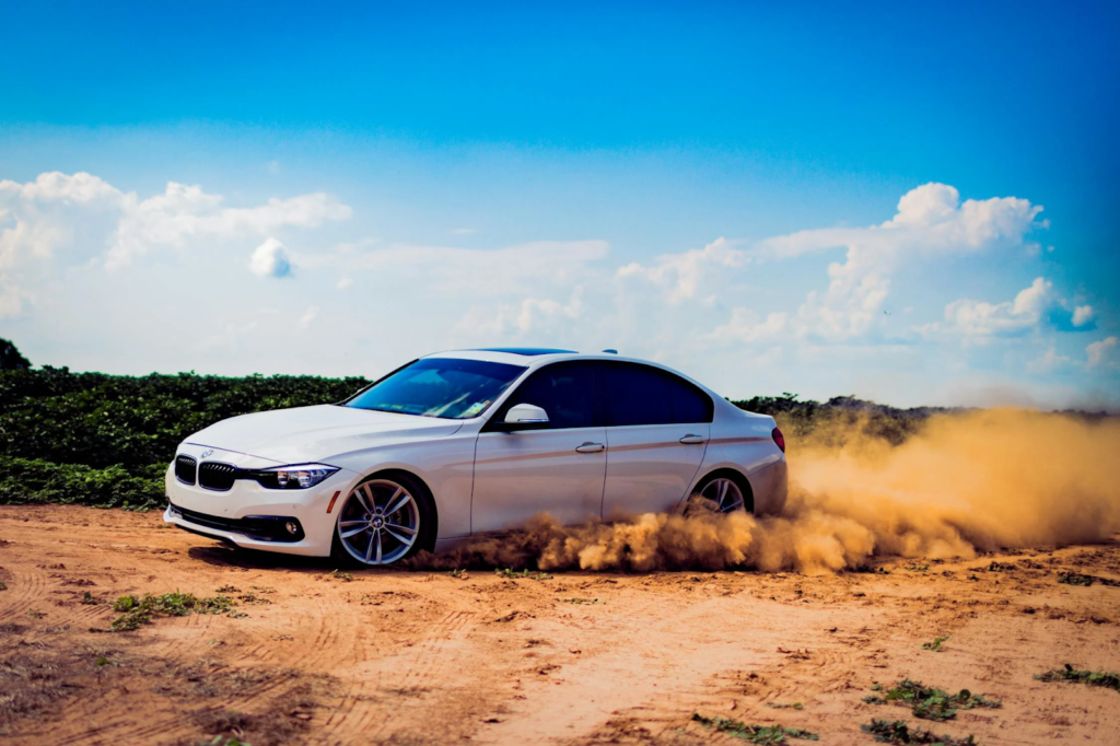 BMW sedan driving on dirt road kicking up dust in an open landscape.