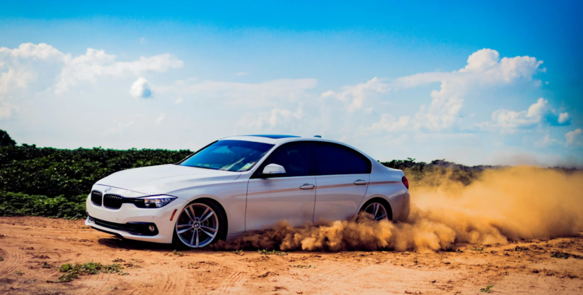 BMW sedan driving on dirt road kicking up dust in an open landscape.