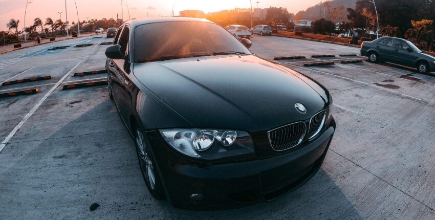 Black BMW parked in a lot during sunset with a scenic background.