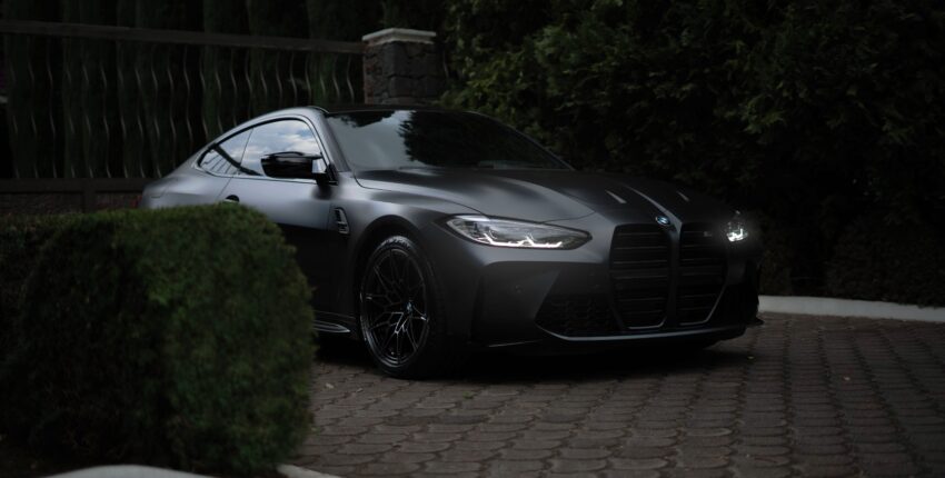 Sleek black BMW M4 parked on a brick driveway with greenery in the background.