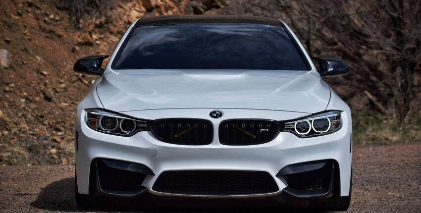White BMW M4 sports car on a dirt road with rocky background.