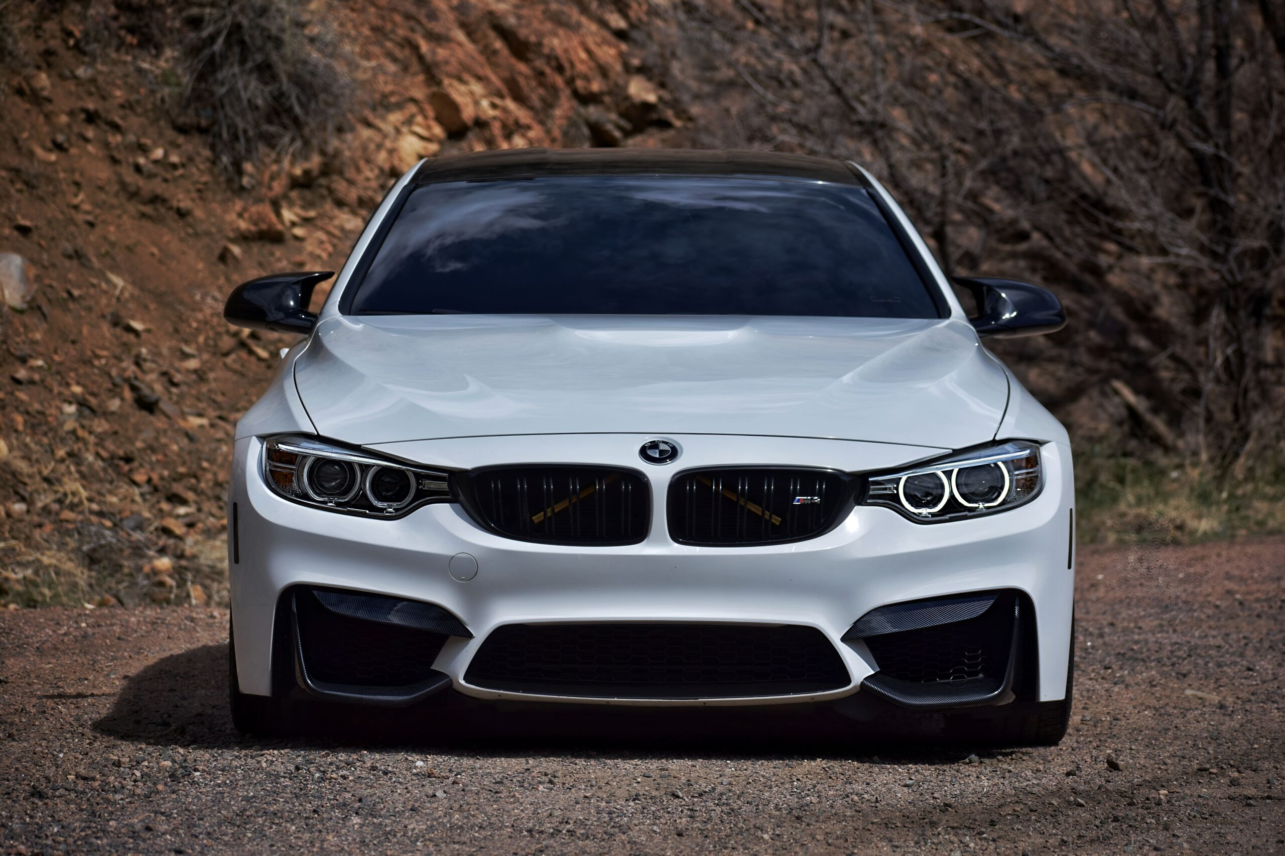 White BMW M4 sports car on a dirt road with rocky background.