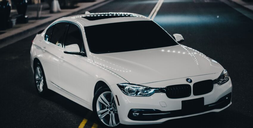 White BMW sedan parked on city street at night with streetlights.