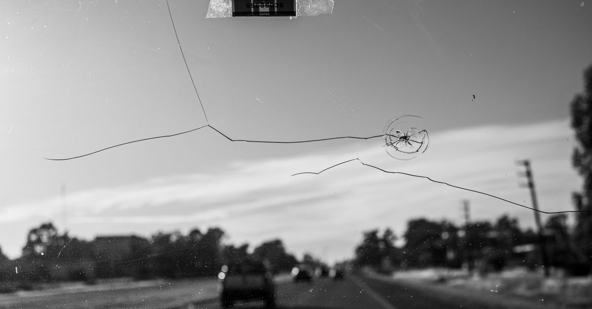 Car driving on road with power lines and trees in background.