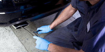 Smog check technician performing vehicle emissions test with equipment and tools.