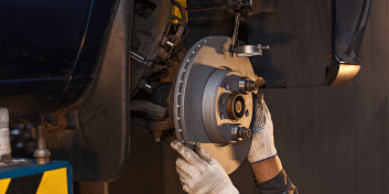 Technician inspecting brake rotor and caliper during brake repair service.