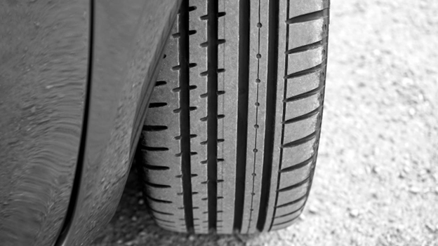 Close-up of a car tire with detailed tread pattern on asphalt.