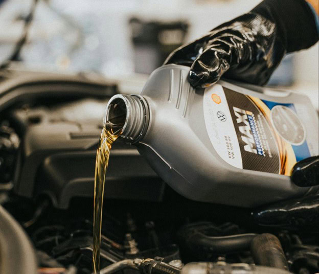 Mechanic pouring transmission fluid into a vehicle engine at Masonic Smog & Repair.
